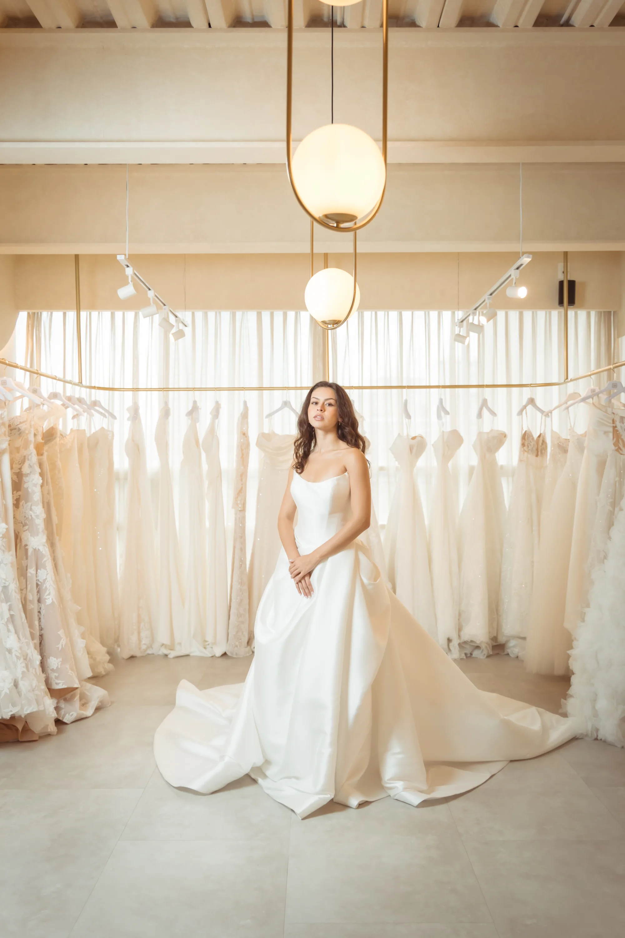 Novia con vestido de satín de silueta A frente al rack de vestidos, fotografía real de Rabling Bridal